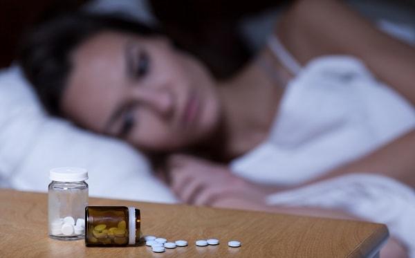 mulher com insônia acordada na cama, olhando para pílulas de dormir na mesinha de cabeceira