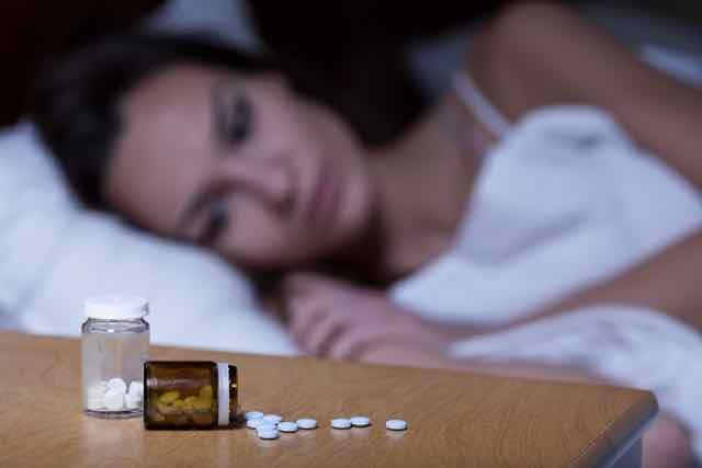 mulher deitada na cama tomando pilulas pra dormir